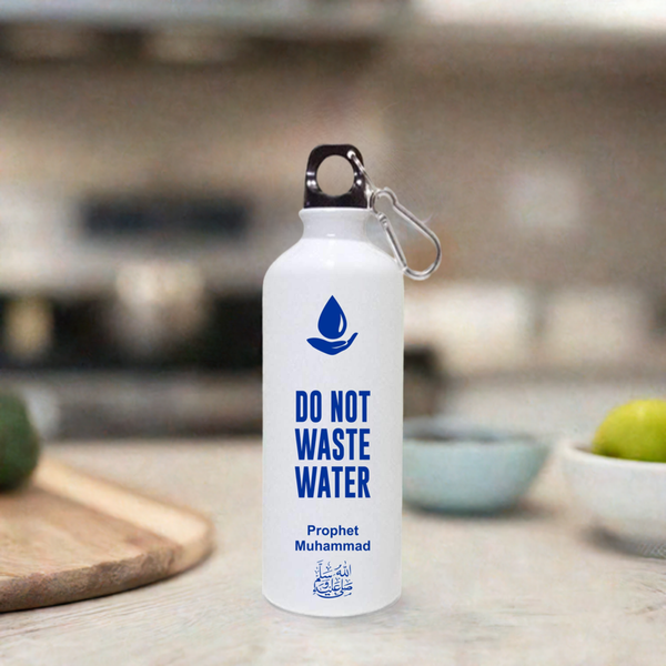 Matte white aluminium water bottle with the quote 'Do Not Waste Water' in blue, UV printed along with an icon of a water droplet and the name 'Prophet Muhammad,' placed on a kitchen countertop with a carabiner clip attached to the bottle's lid.