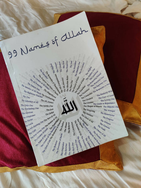 99 Names of Allah book by Rawdah Pearls, featuring the names of Allah in a circular design around the word 'Allah' in the center. The book is displayed on a red and gold pillow.